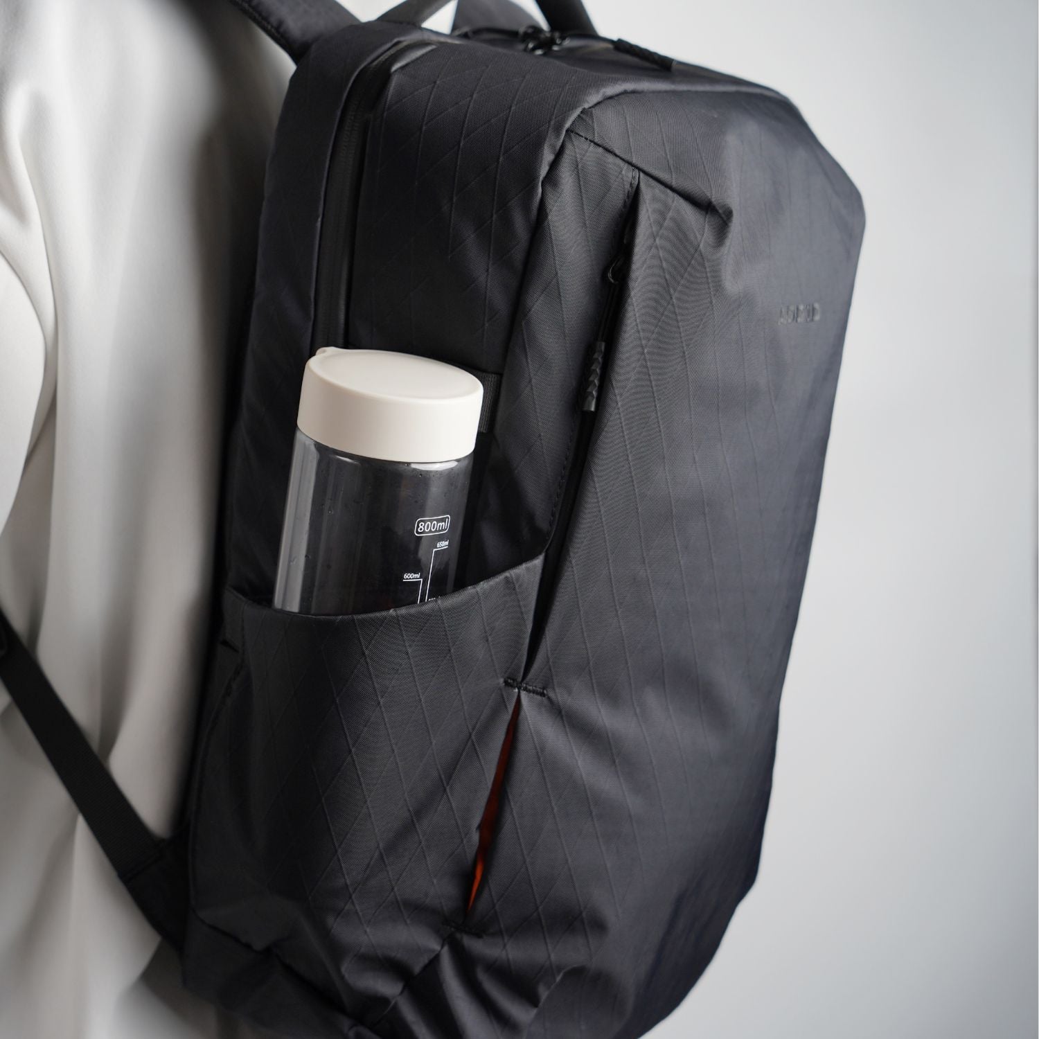 Side view of ADD1D D2D Essential Backpack showing expandable water bottle pocket